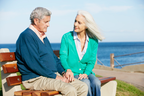 Senior woman sits with senior man on park bench.